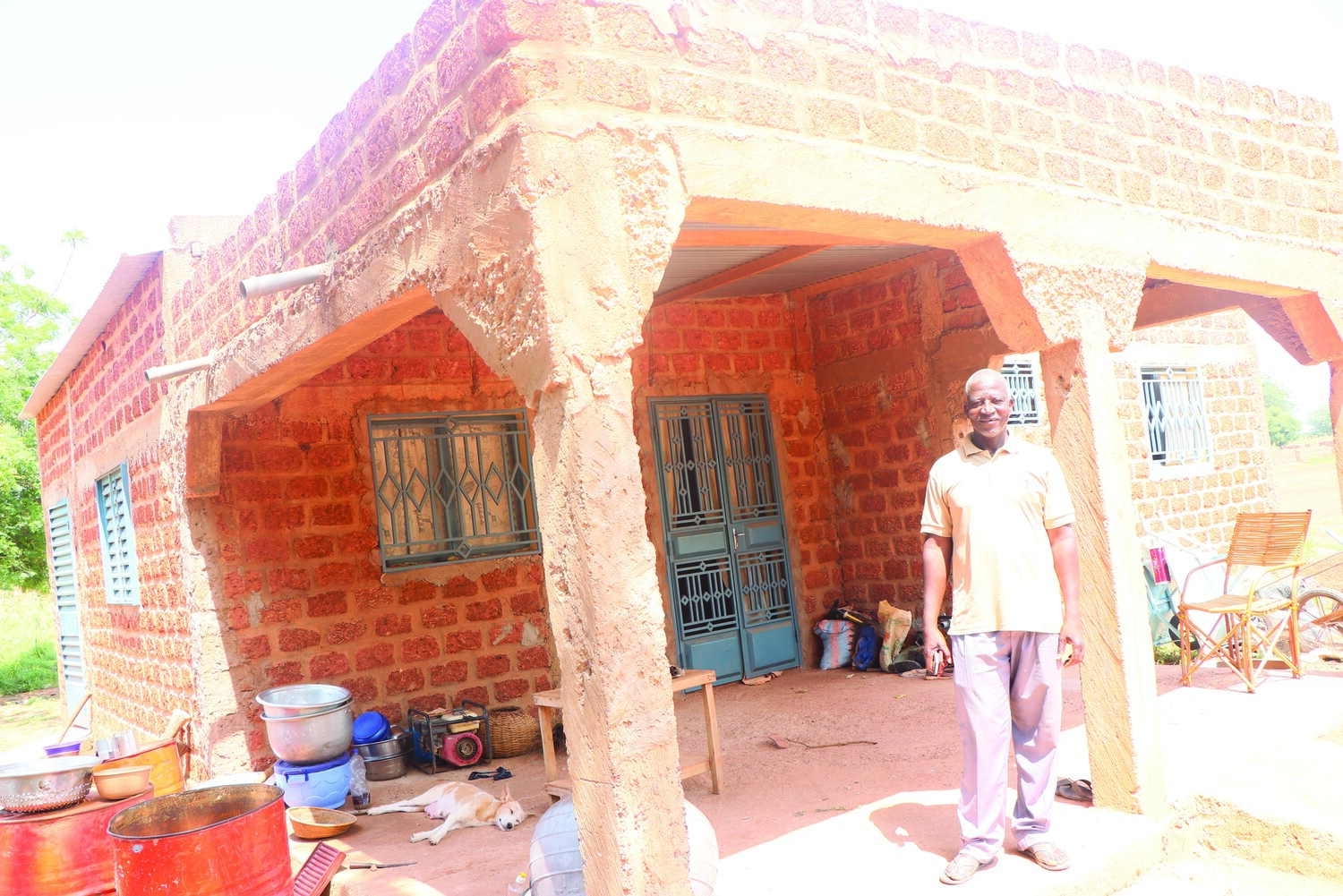 Joël stands in front of his new brick house built with his increased income.